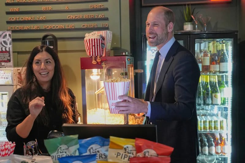 Woman in black top and man in dark suit holding popcorn bucket, cinema concession stand.