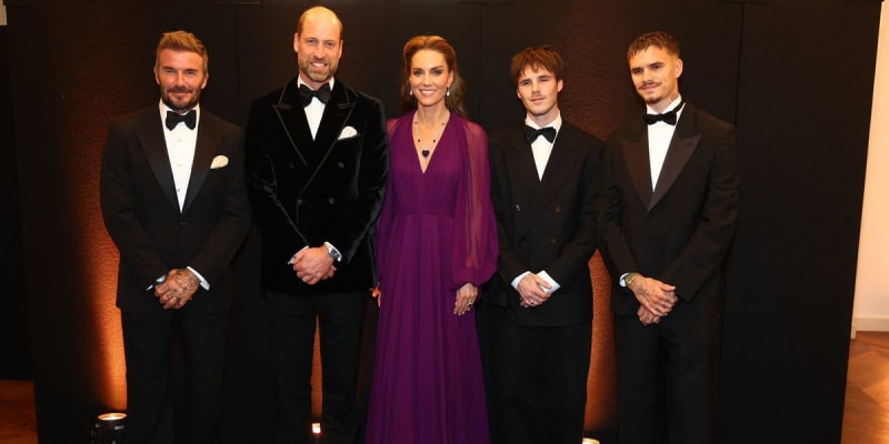 Five people in formal attire stand together against a dark background at an elegant event.