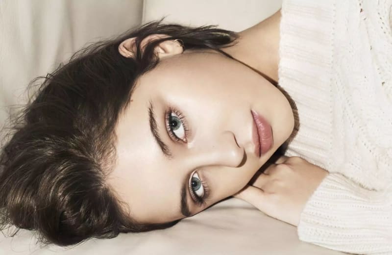 Woman in white knit sweater, lying down, close-up face shot.