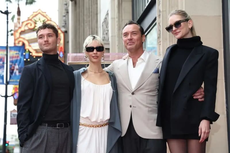 Two men and two women posing together on Hollywood Walk of Fame, one in white dress, one in black blazer.