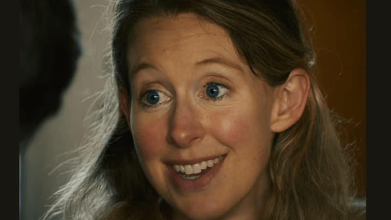 A woman with brown hair and blue eyes smiles widely at the camera with an surprised or delighted expression.