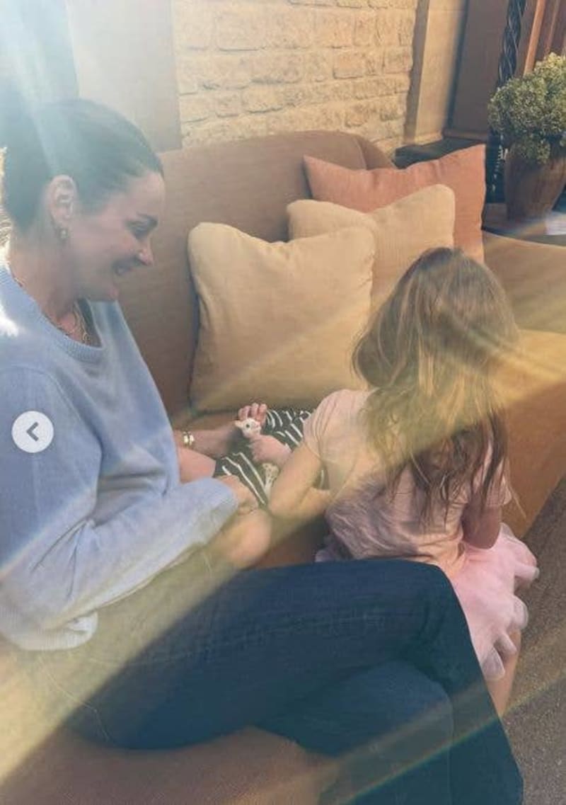 An adult and child sitting together on a tan couch, smiling and looking at a small plant or seedling in their hands.