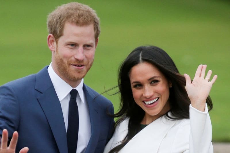 Two people in formal attire waving at the camera against a green background.