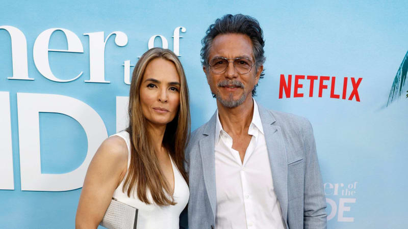 Two people posing at a Netflix event premiere against a blue backdrop with Netflix logo visible.