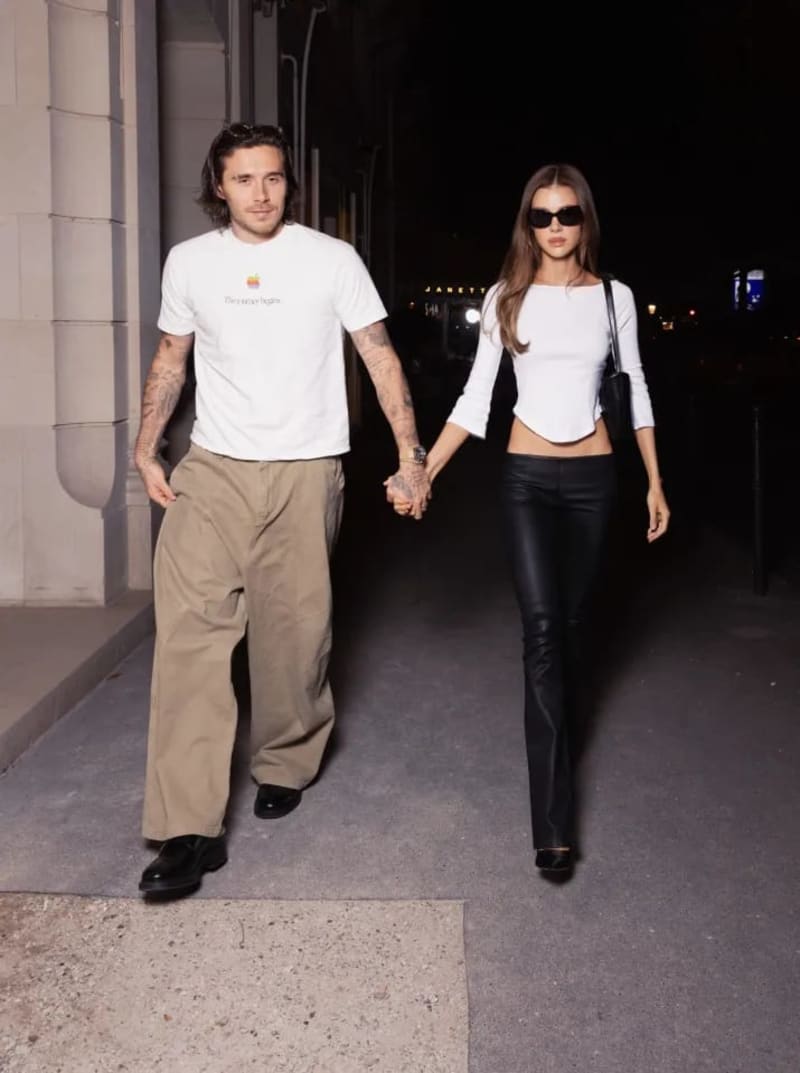 Two people holding hands walking down a nighttime urban street, both wearing white tops and dark bottoms.