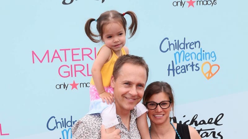 A man holds a young child on his shoulders while standing next to a smiling woman at a charity event backdrop.