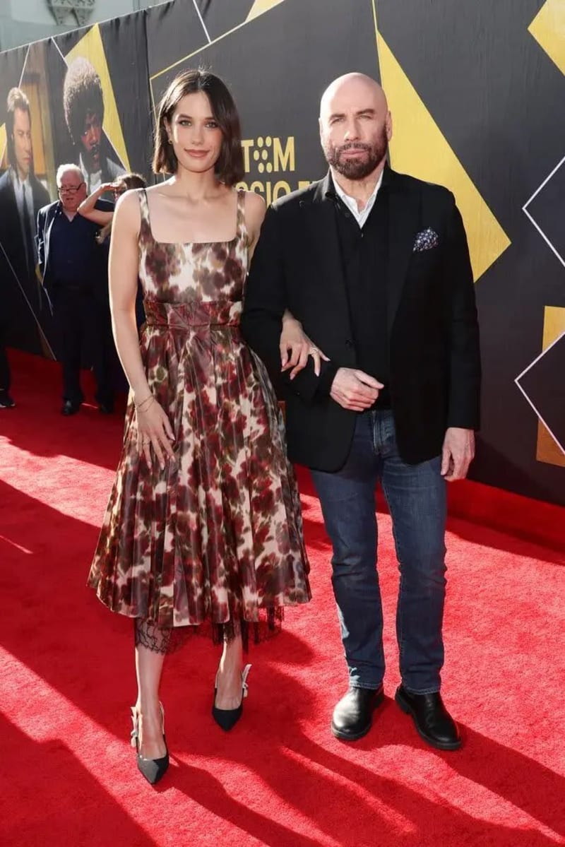 Woman in floral midi dress and man in black blazer and jeans on red carpet.