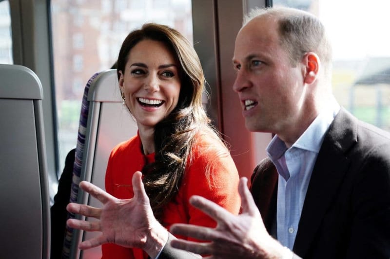 Two people in formal attire smile while having a conversation in a high-rise building with city views visible through windows.