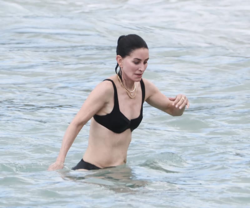 Woman in black bikini wading in ocean water.