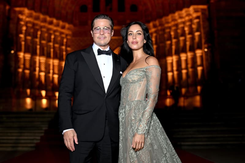 Two people in formal attire pose together at an elegant event with ornate golden columns illuminated in the background.