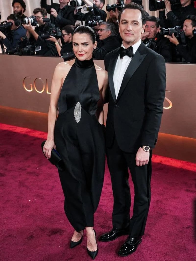 Two people in formal black attire pose together on a red carpet at what appears to be a major entertainment event, surrounded by photographers.