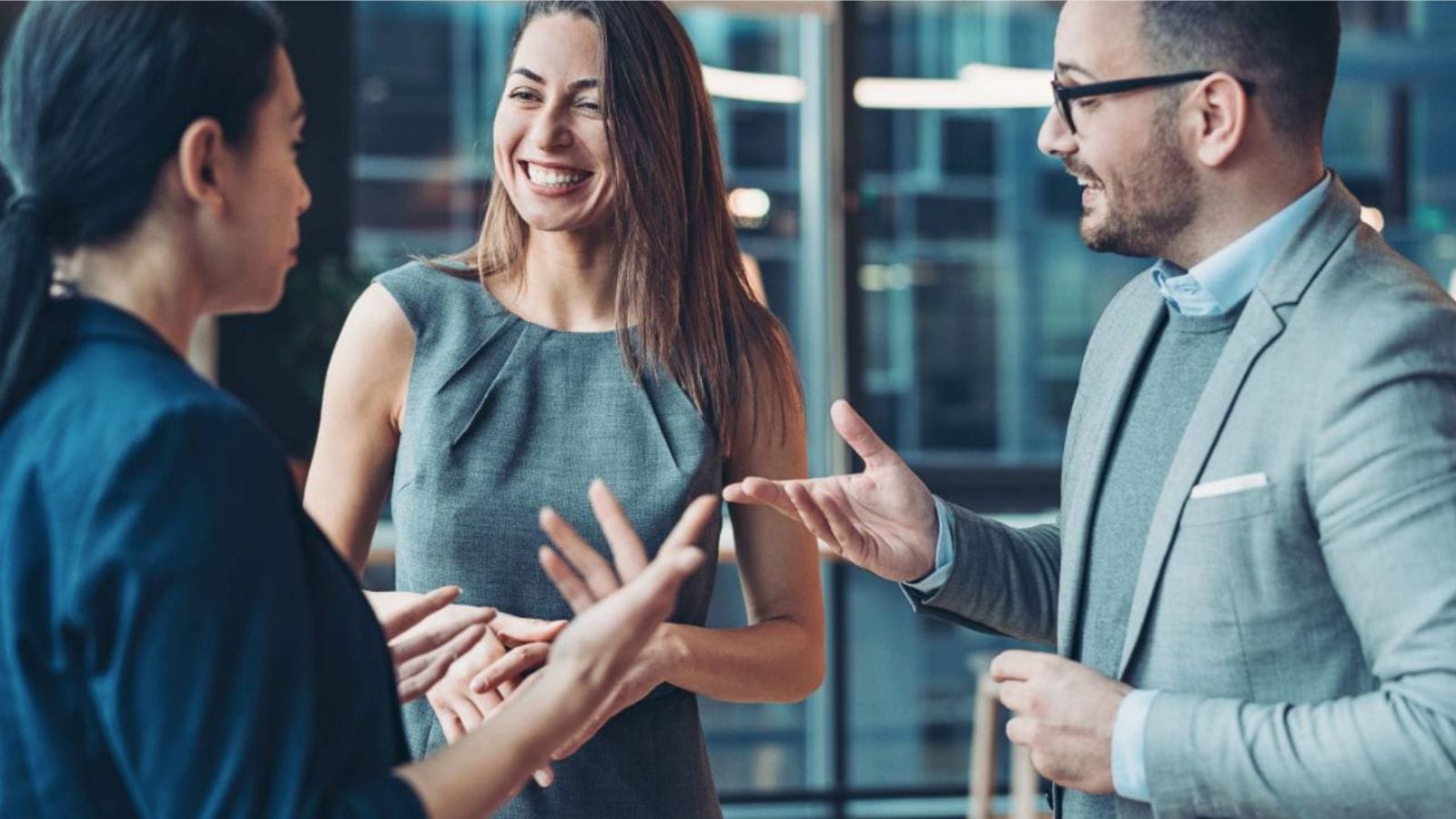 Two women and a man in business attire having an engaging discussion about work.