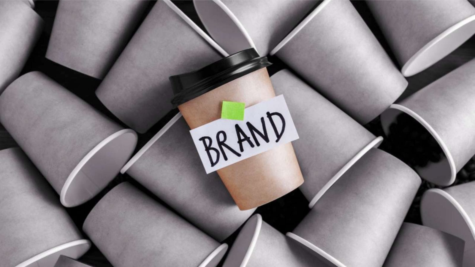 A pile of grey coffee cups with one brown and black one on top with a taped label with the word "brand".