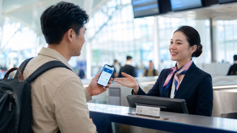 Voyageur présentant sa réservation de vol sur smartphone à un agent au comptoir d'enregistrement