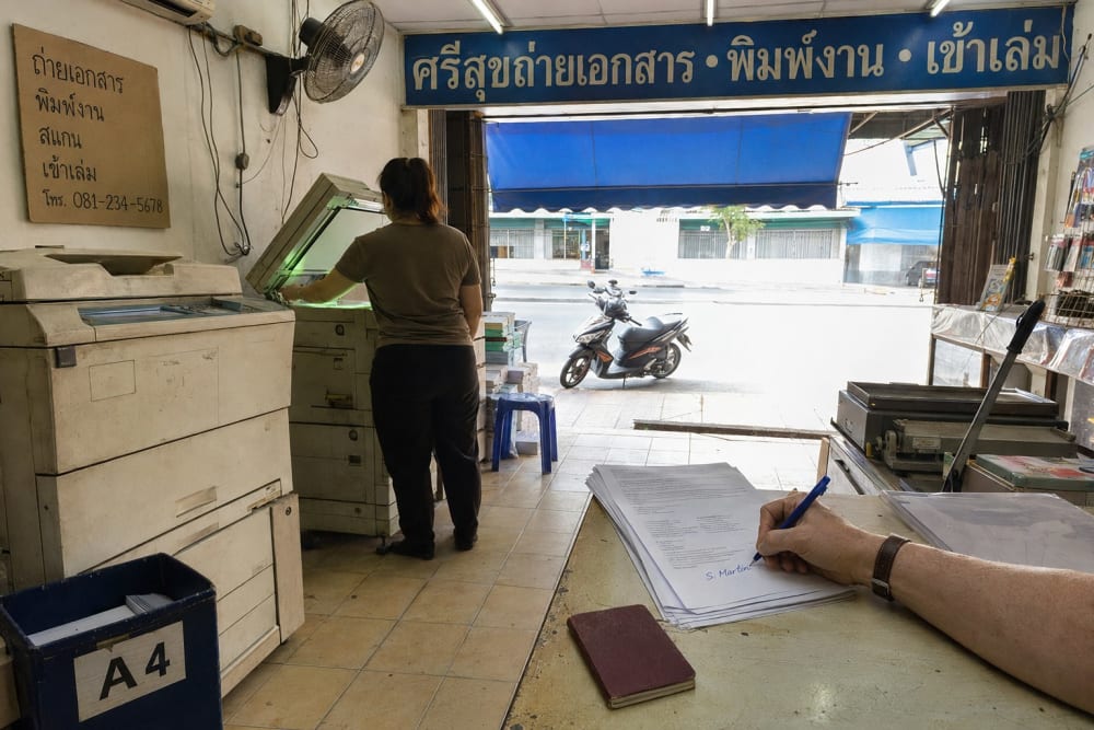 Main d'un client signant une pile de photocopies sur le comptoir d'une boutique de photocopie thaïlandaise ouverte sur la rue