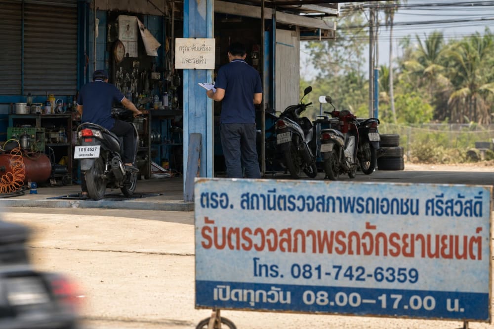 Scooter posé sur un banc à rouleaux dans une station de contrôle technique de bord de route, technicien accroupi de dos