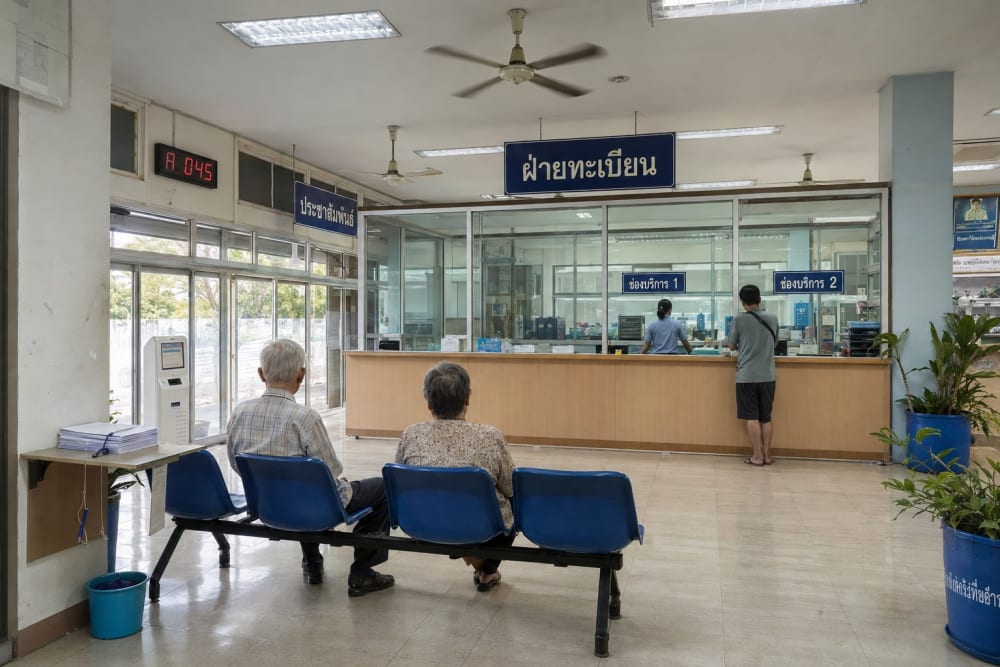Salle d'attente d'un bureau de district thaïlandais, comptoirs vitrés et panneaux en thaï, le matin
