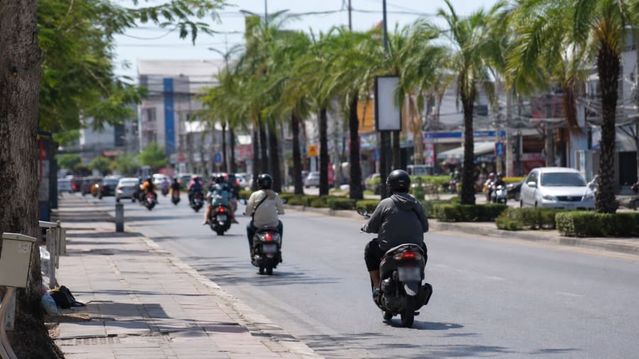 Circulation de scooters sur une avenue de Pattaya, conducteurs casqués vus de dos