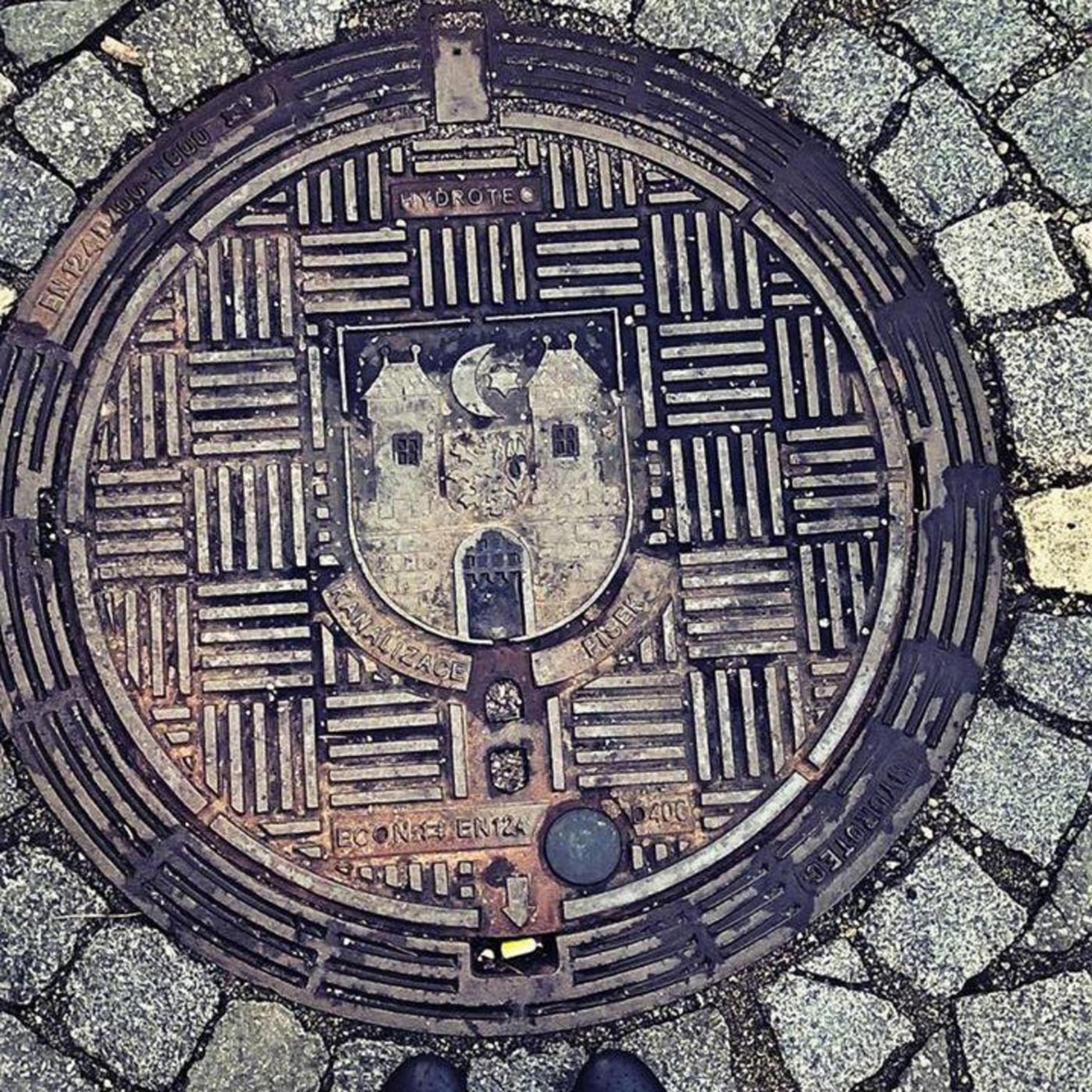 Dlažba z drobných kostek obklopuje kruhový exemplář s výrazným geometrickým vzorem mřížky. Uprostřed je patrný stylizova in Písek, Czechia — CoverSpot