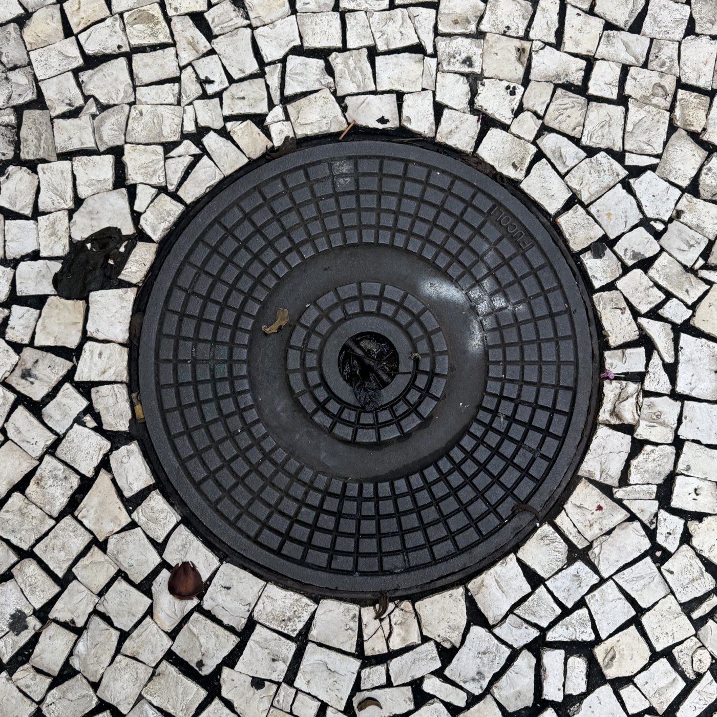 Vzácný exemplář kruhového poklopu, zasazený do mozaiky z bílých dlažebních kostek, vykazuje precizní geometrický vzor so in Santa Luzia, Madeira, Portugal — CoverSpot