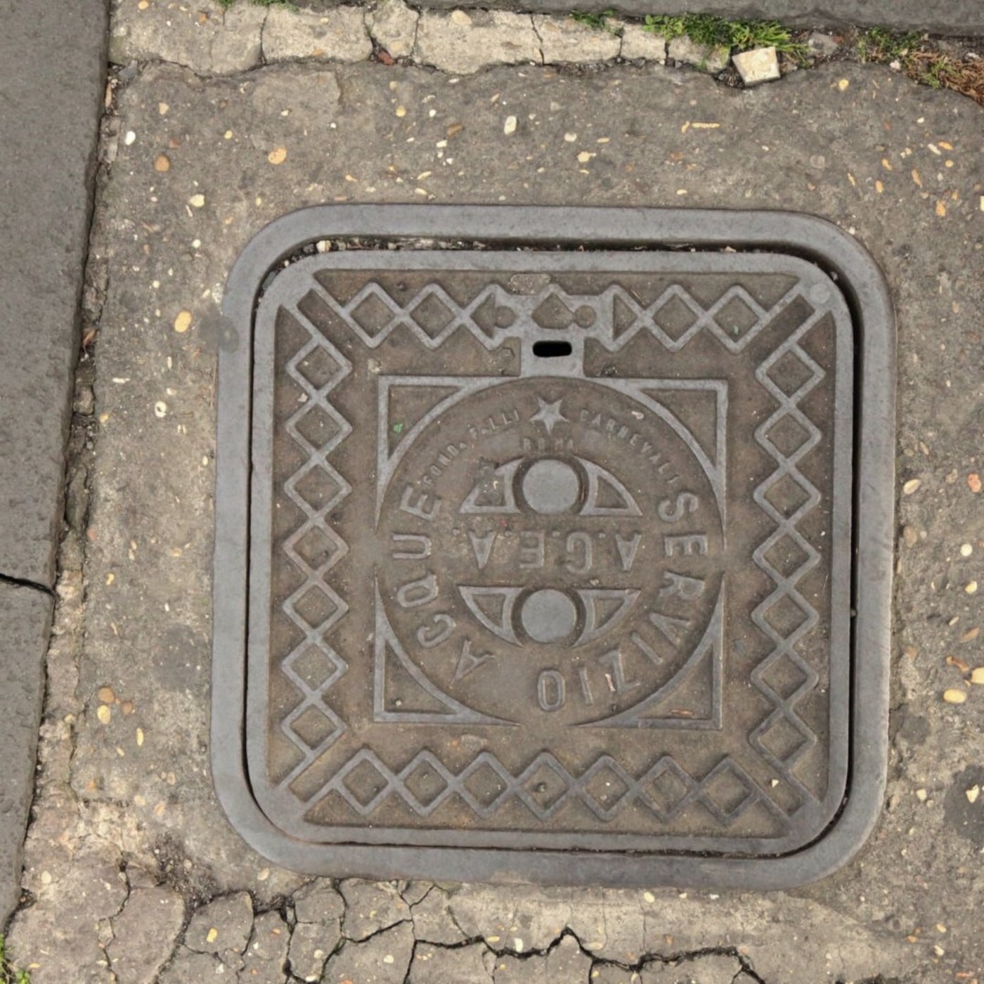 Centrální kruhový motiv s nápisem 'ACQUE E SERVIZIO' dominuje tomuto čtvercovému exempláři, obklopenému opakujícím se di in Rome, Italy — CoverSpot