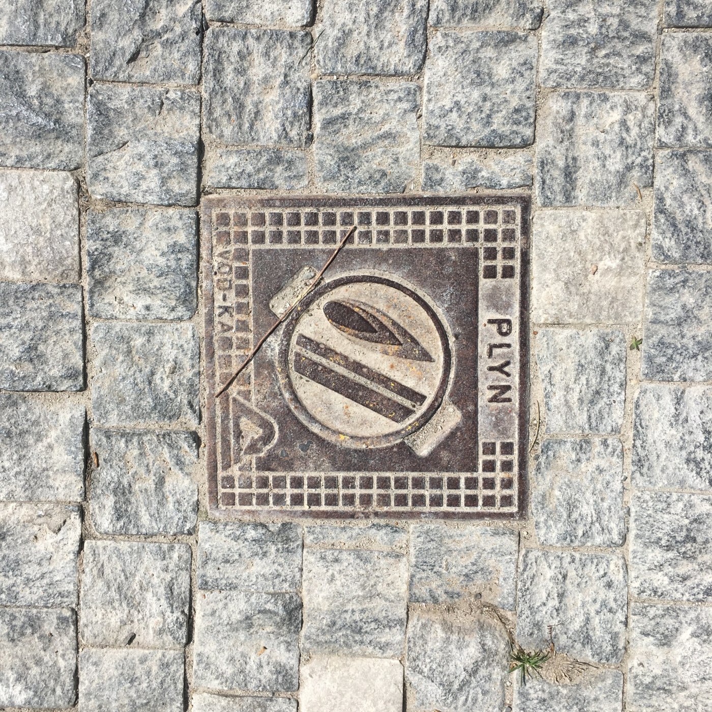 Centrální kruhový motiv s abstraktním symbolem dominuje tomuto čtvercovému exempláři, zasazenému do dlažebních kostek. V in Praha, Czechia — CoverSpot