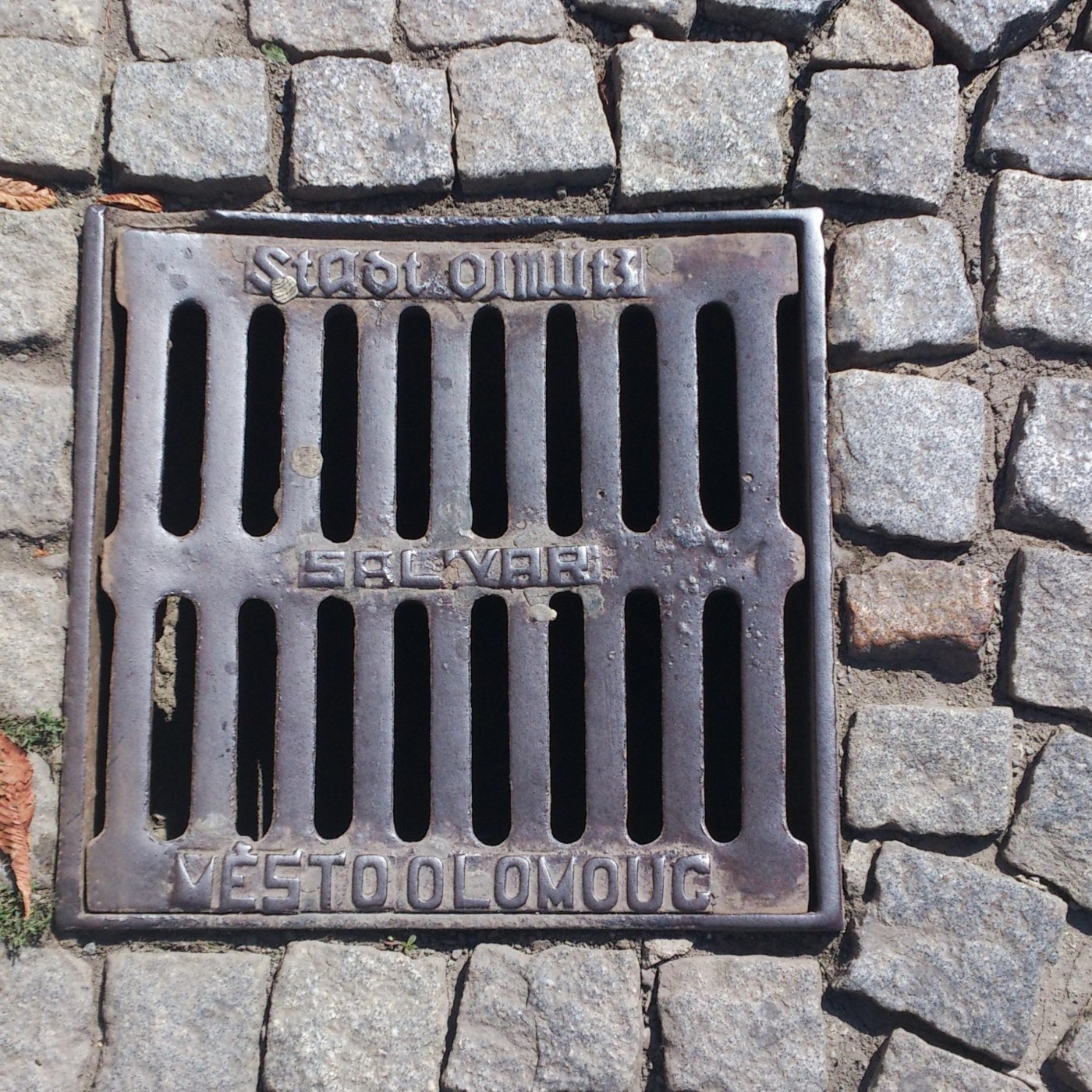 Na povrchu čtvercového odvodňovacího roštu jsou patrné nápisy odkazující na město Olomouc. Přítomnost staršího německého in Olomouc, Olomoucký, Czechia — CoverSpot