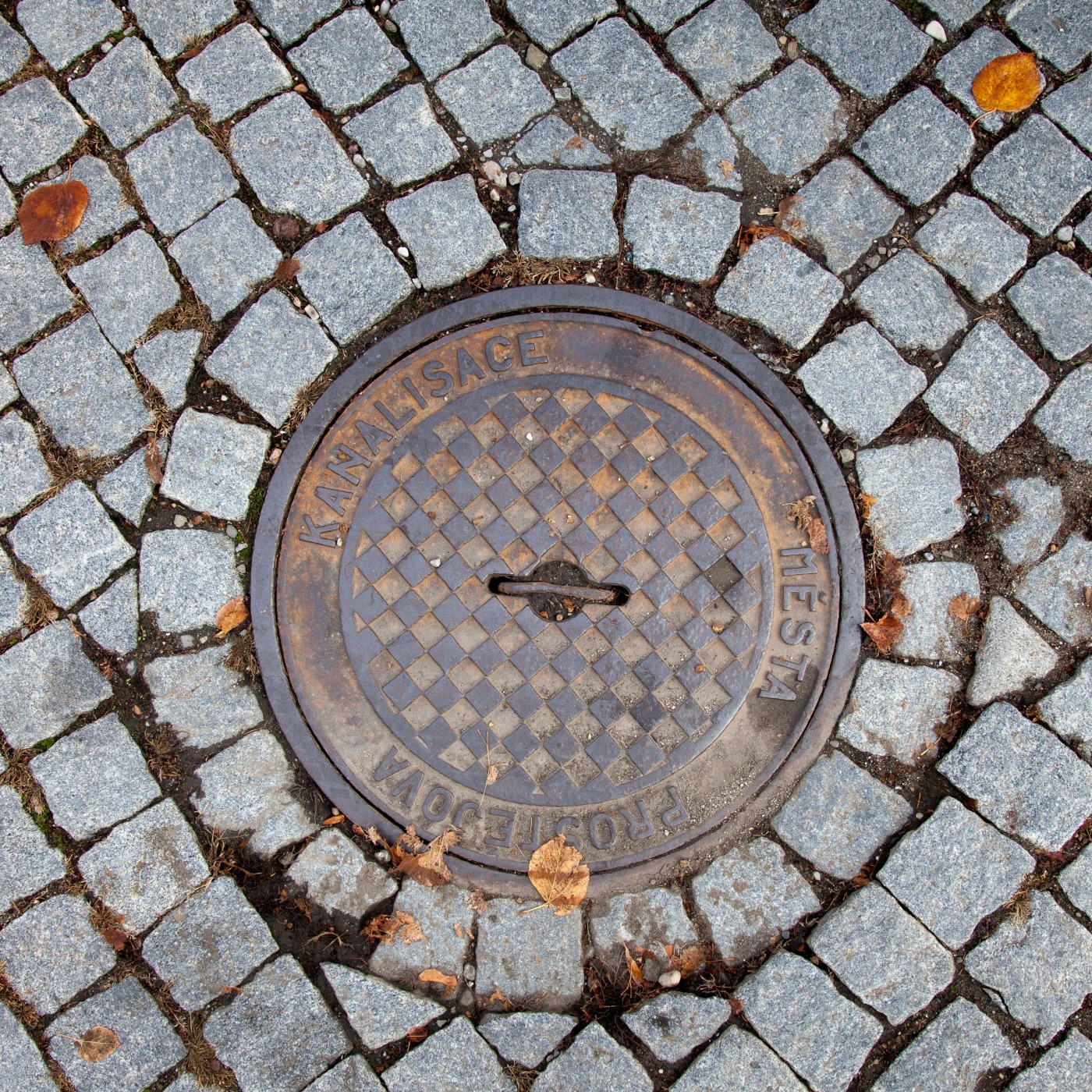 Centrální kruhový artefakt, obklopený dlažebními kostkami, vykazuje na svém povrchu geometrický šachovnicový vzor, což n in Prostějov, Czechia — CoverSpot