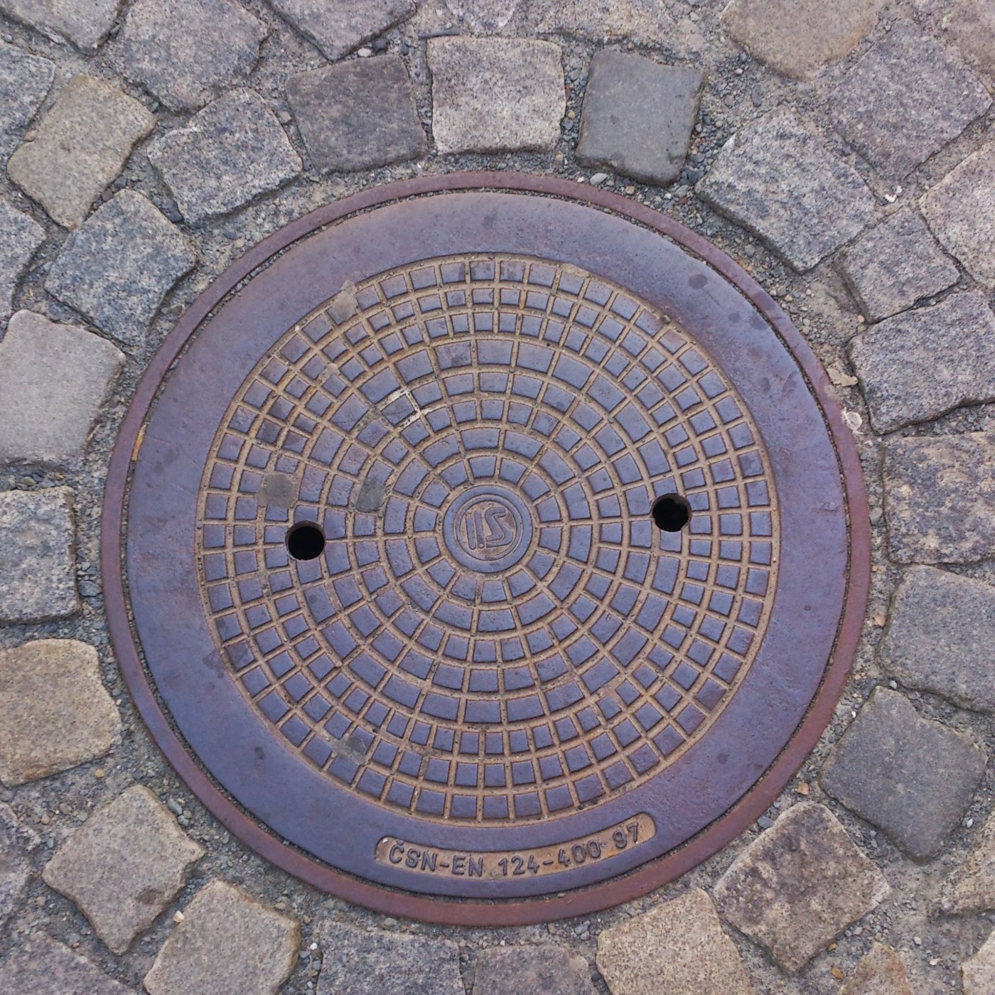 Kruhový mřížkový vzor, uspořádaný do soustředných kružnic, dominuje tomuto exempláři městské infrastruktury. V jeho stře in Olomouc, Olomoucký, Czechia — CoverSpot