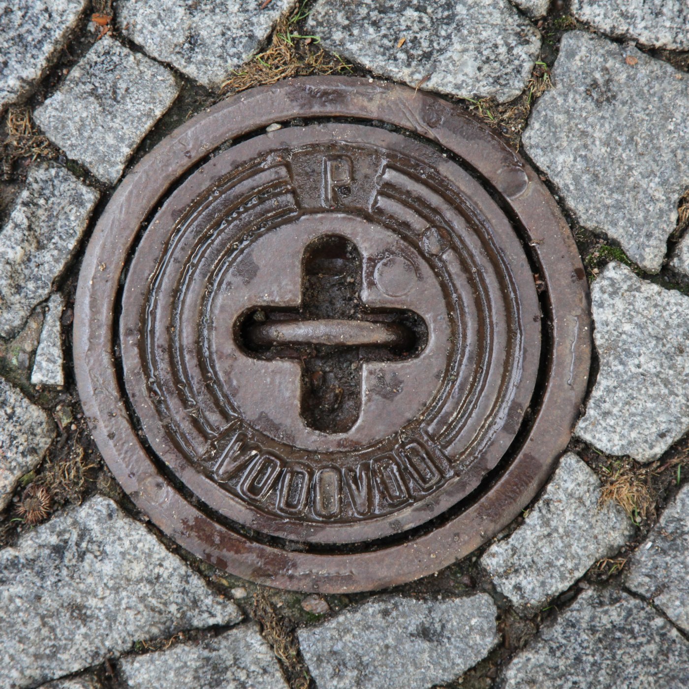 Na povrchu kruhového kovového disku dominuje centrální křížový motiv, obklopený soustřednými kružnicemi a hrubou dlažbou in Hradec Králové, Czechia — CoverSpot