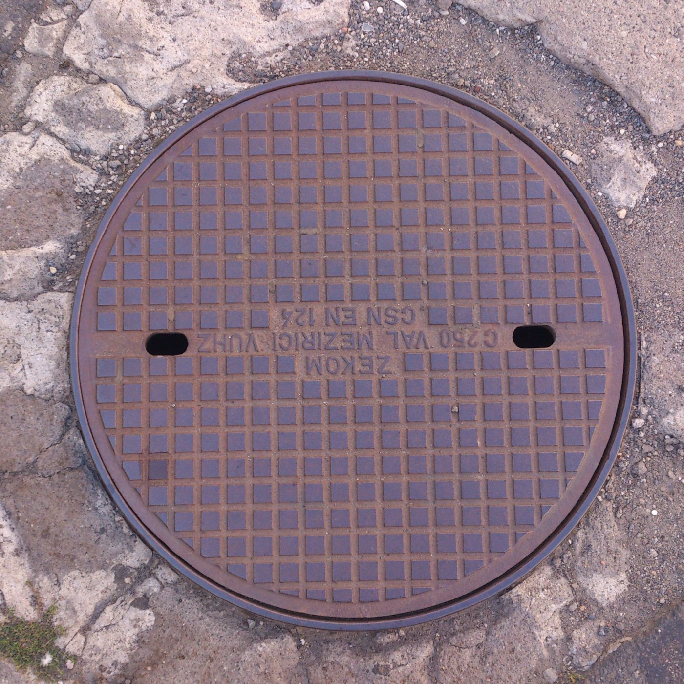 Pravidelná mřížka čtverců pokrývá povrch tohoto kruhového exempláře, což naznačuje jeho robustní funkční design. Nápisy  in Olomouc, Olomoucký, Czechia — CoverSpot