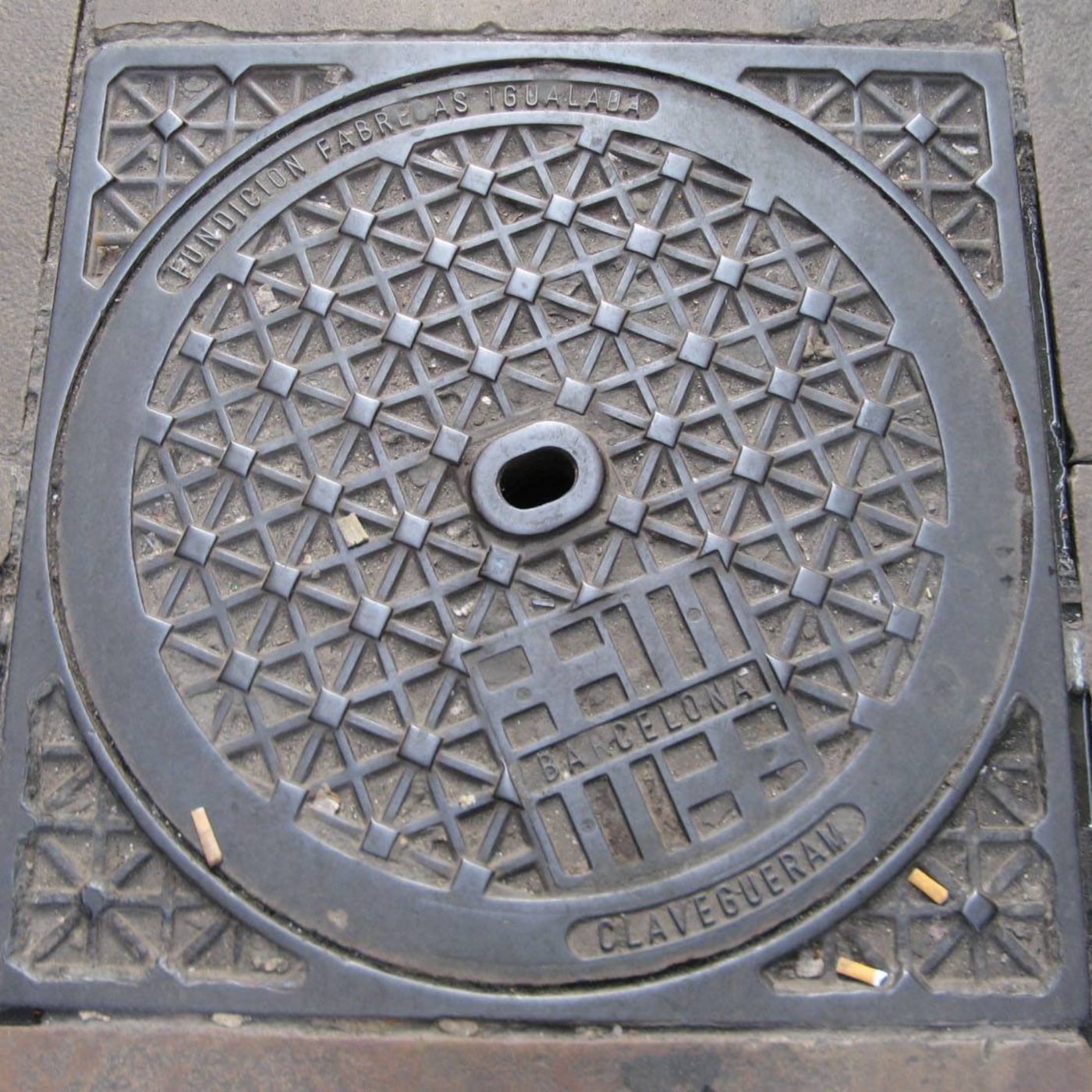 Složitý geometrický vzor trojúhelníků a čtverců dominuje tomuto exempláři městské infrastruktury. Kruhový design je obkl in Barcelona, Catalonia, Spain — CoverSpot