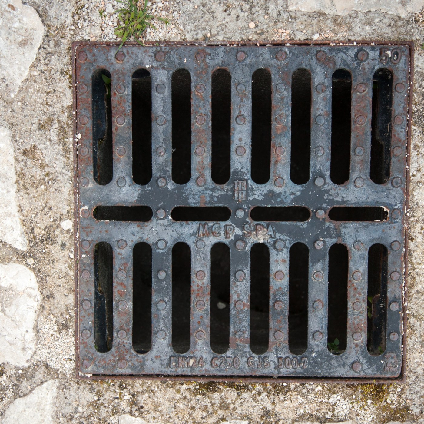 Na povrchu čtvercového odvodňovacího roštu dominuje výrazná patina rzi, která svědčí o dlouhodobé expozici povětrnostním in Matera, Italy — CoverSpot