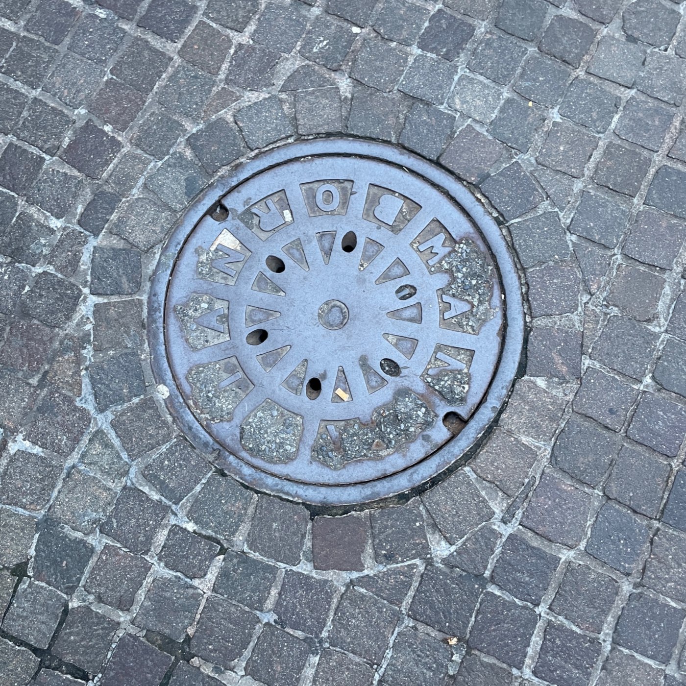 Centrální kruhový artefakt, zasazený do mozaiky z dlažebních kostek, vykazuje radiální segmentaci a perforace, což nazna in Hoboken, New Jersey, United States — CoverSpot