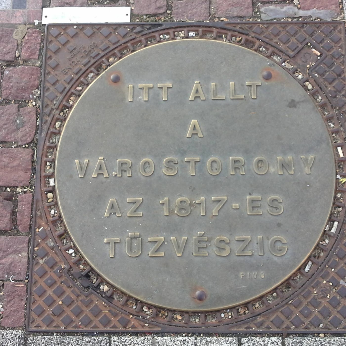 Uprostřed dlážděné cesty leží kruhová mosazná deska, která svým nápisem v maďarštině připomíná historickou událost. Zlat in Szombathely, Hungary — CoverSpot