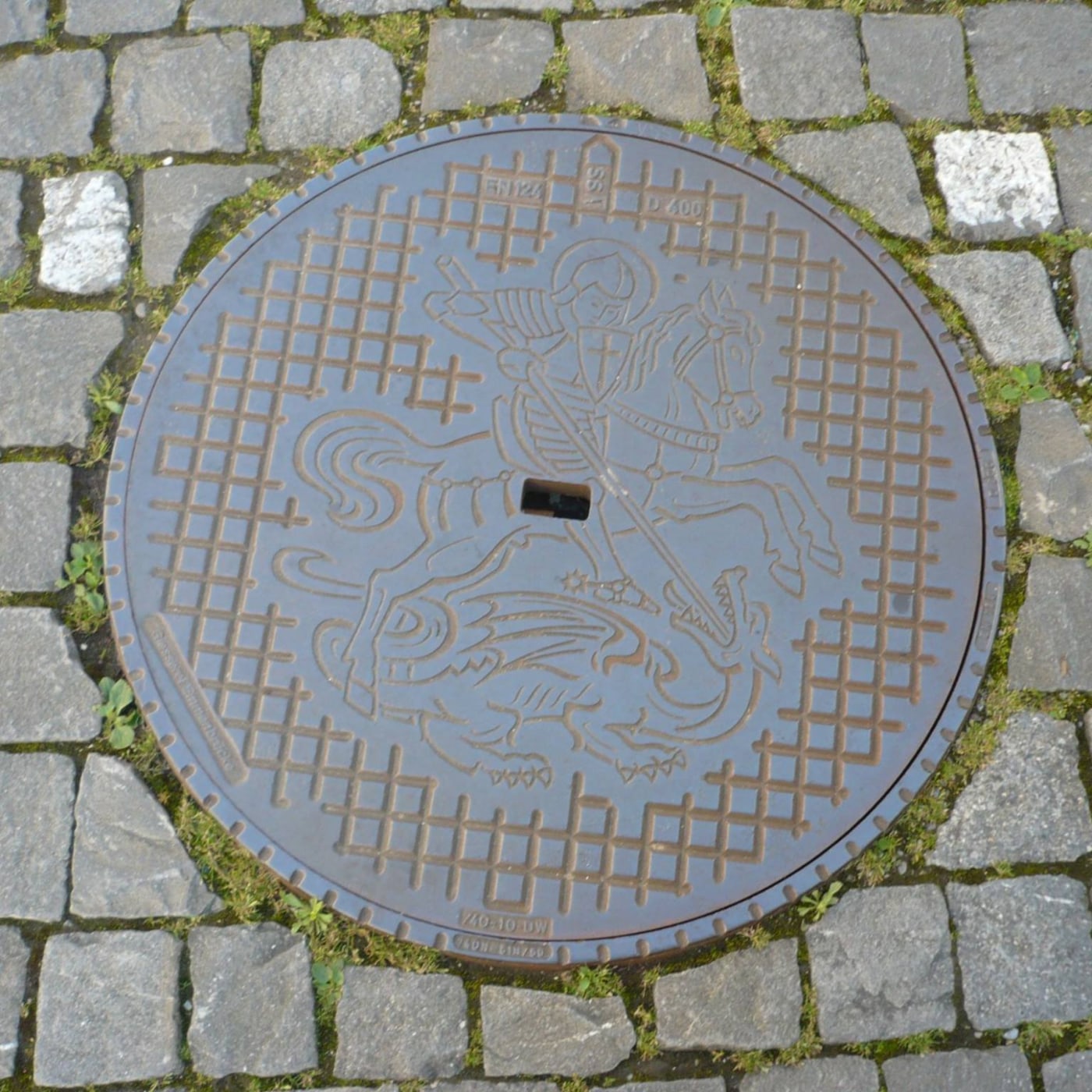 Jezdec na koni probodávající draka tvoří ústřední reliéfní motiv tohoto kruhového poklopu, obklopeného pravidelným mřížk in Stein am Rhein, Switzerland — CoverSpot