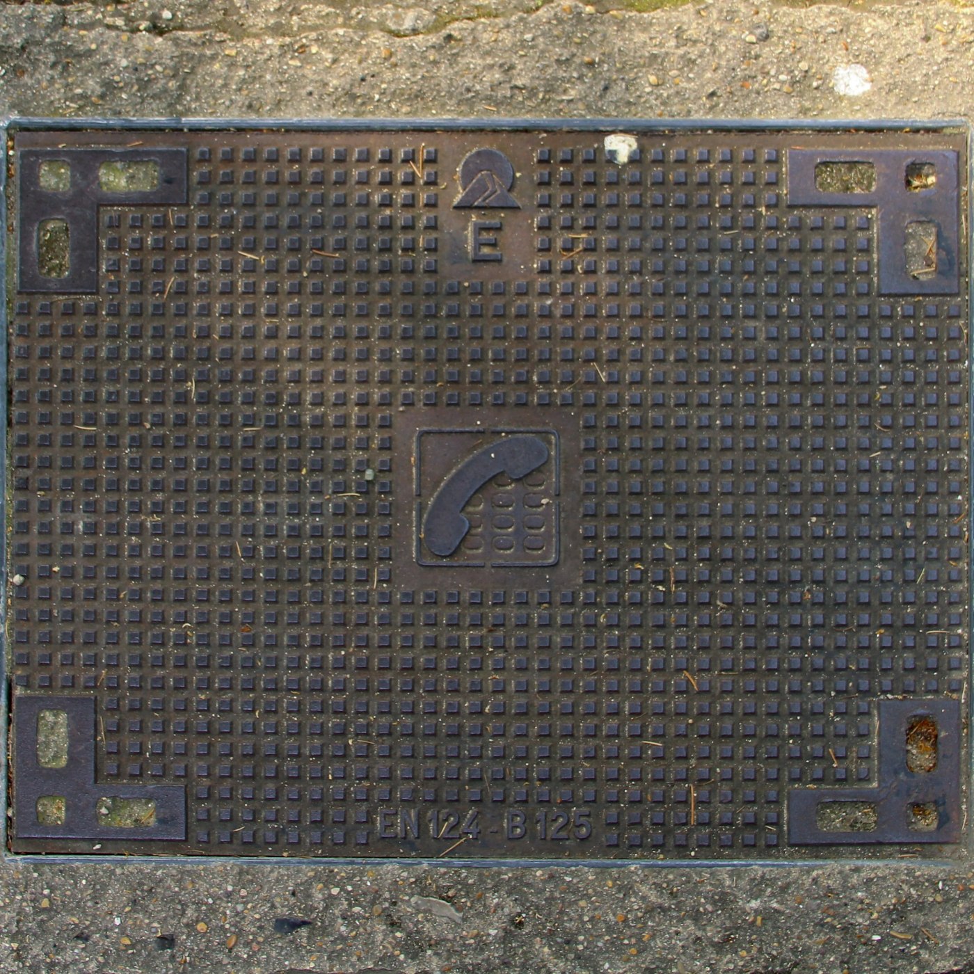 Na tmavém kovovém povrchu dominuje pravidelný mřížkový vzor malých čtverců, doplněný centrálním symbolem telefonního slu in Paris, Île-de-France, France — CoverSpot