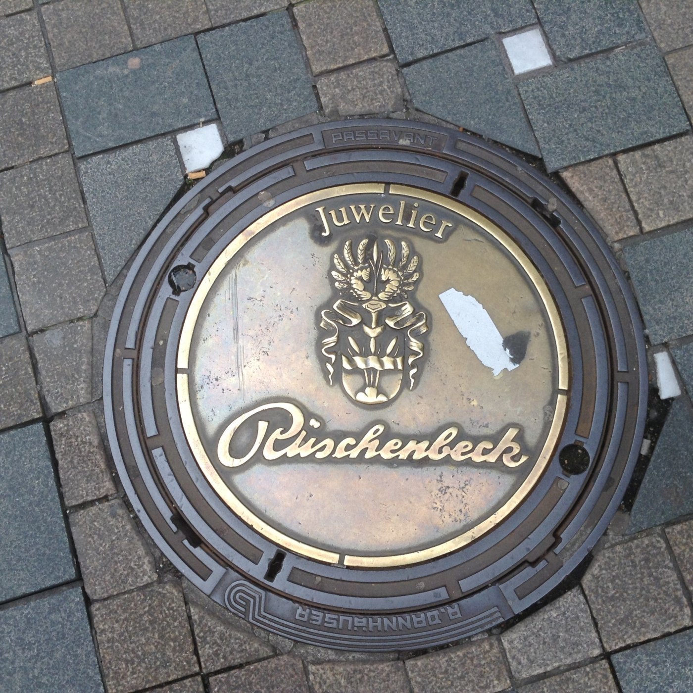 Uprostřed tohoto exempláře se nachází výrazný mosazný medailon s nápisem „Juwelier Rüschenbeck“ a stylizovaným erbem, co in Dortmund, North Rhine-Westphalia, Germany — CoverSpot