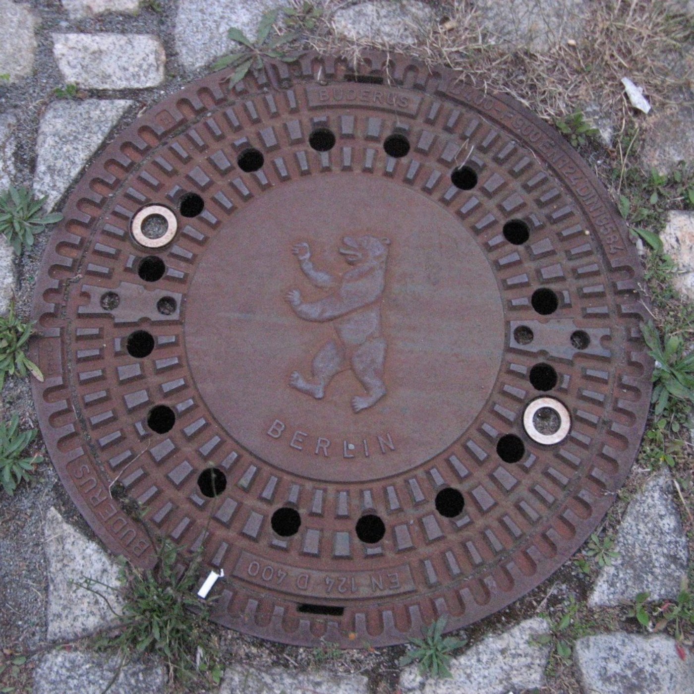 Centrální reliéf medvěda, heraldického symbolu Berlína, dominuje tomuto exempláři litinového poklopu. Okolní prstenec ne in Berlin, State of Berlin, Germany — CoverSpot