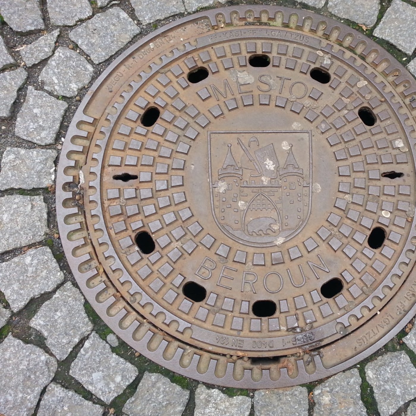 Tento kruhový litinový poklop, zasazený do mozaiky šedých dlažebních kostek, nese hrdě znak města Beroun. Uprostřed se v in Poděbrady, Central Bohemia, Czechia — CoverSpot