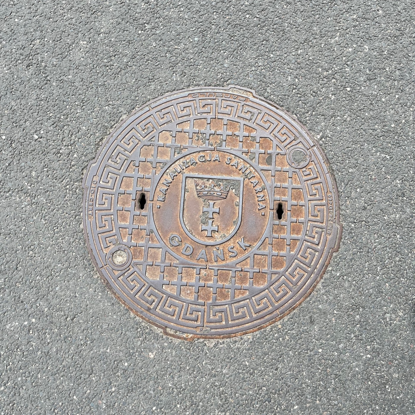 Centrální erb města Gdaňsk, s korunou a dvěma kříži, dominuje tomuto exempláři litinového poklopu, který představuje fas in Środmieście, Pomerania, Poland — CoverSpot