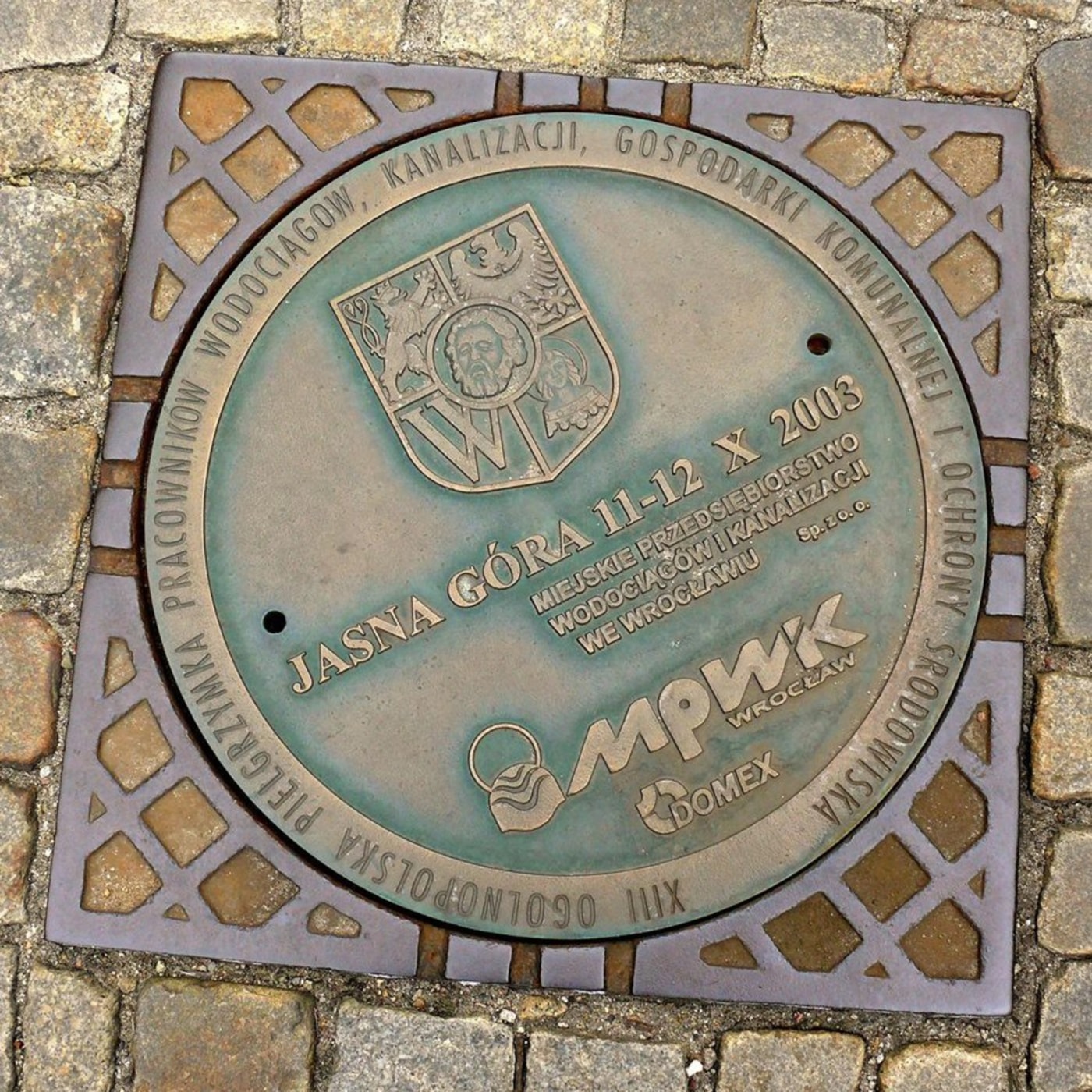 Na patinovaném povrchu kruhového poklopu dominují nápisy v polštině, připomínající XIII. celopolskou pouť pracovníků vod in Wrocław, Poland — CoverSpot