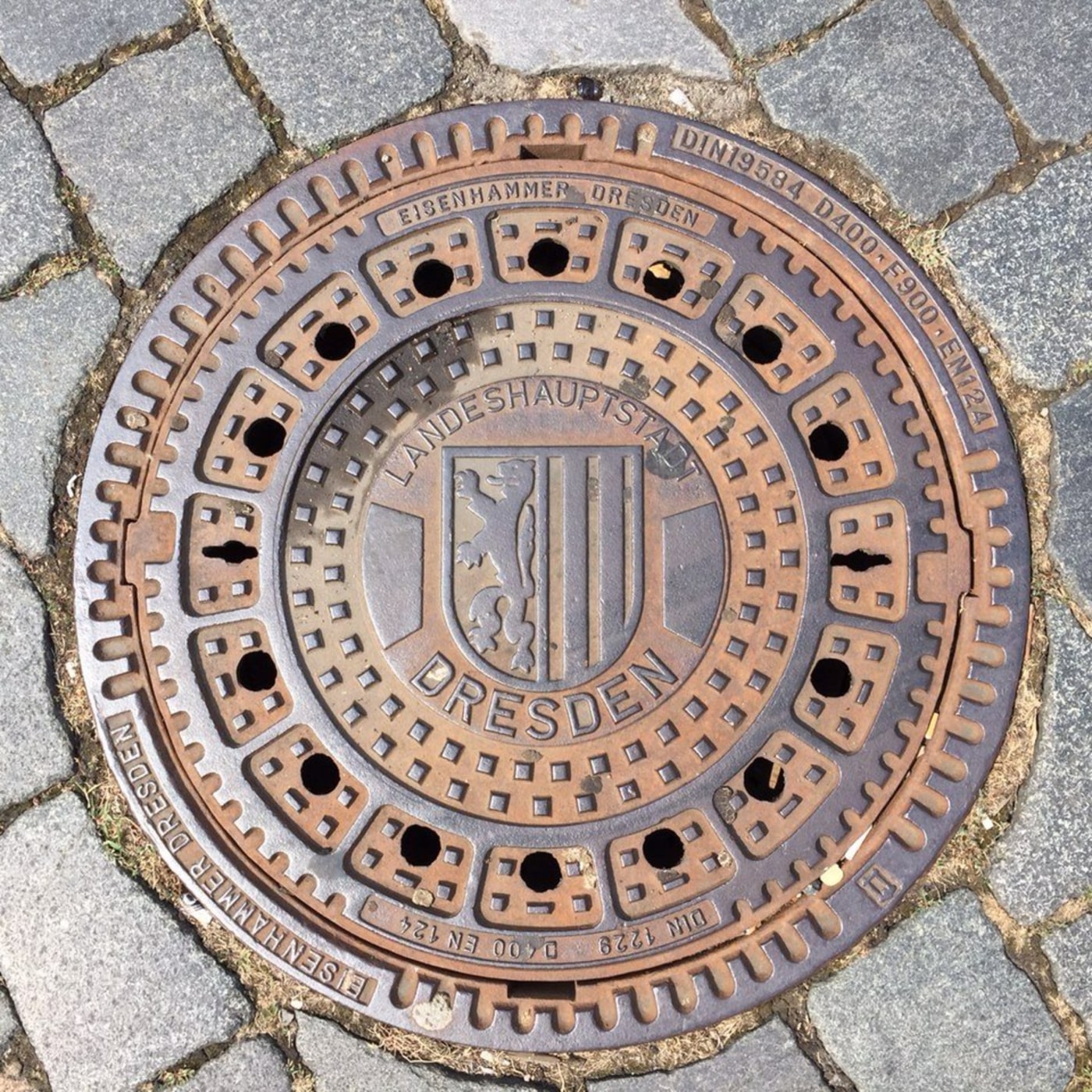 Na povrchu tohoto kruhového litinového exempláře dominuje centrální erb města Drážďany, obklopený textem "LANDESHAUPTSTA in Dresden, Germany — CoverSpot