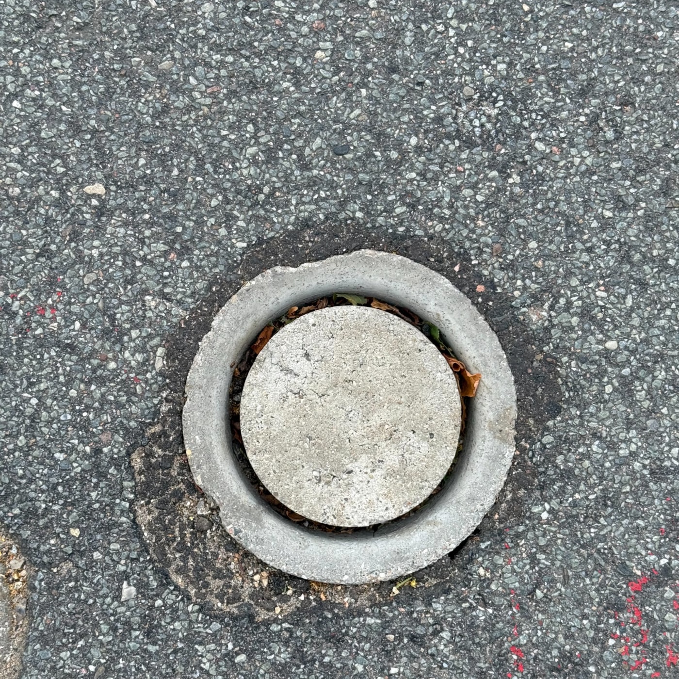 Povrch asfaltové vozovky je narušen kruhovým betonovým prvkem, který slouží jako přístupový bod k podzemní infrastruktuř in Billund, South Denmark, Denmark — CoverSpot