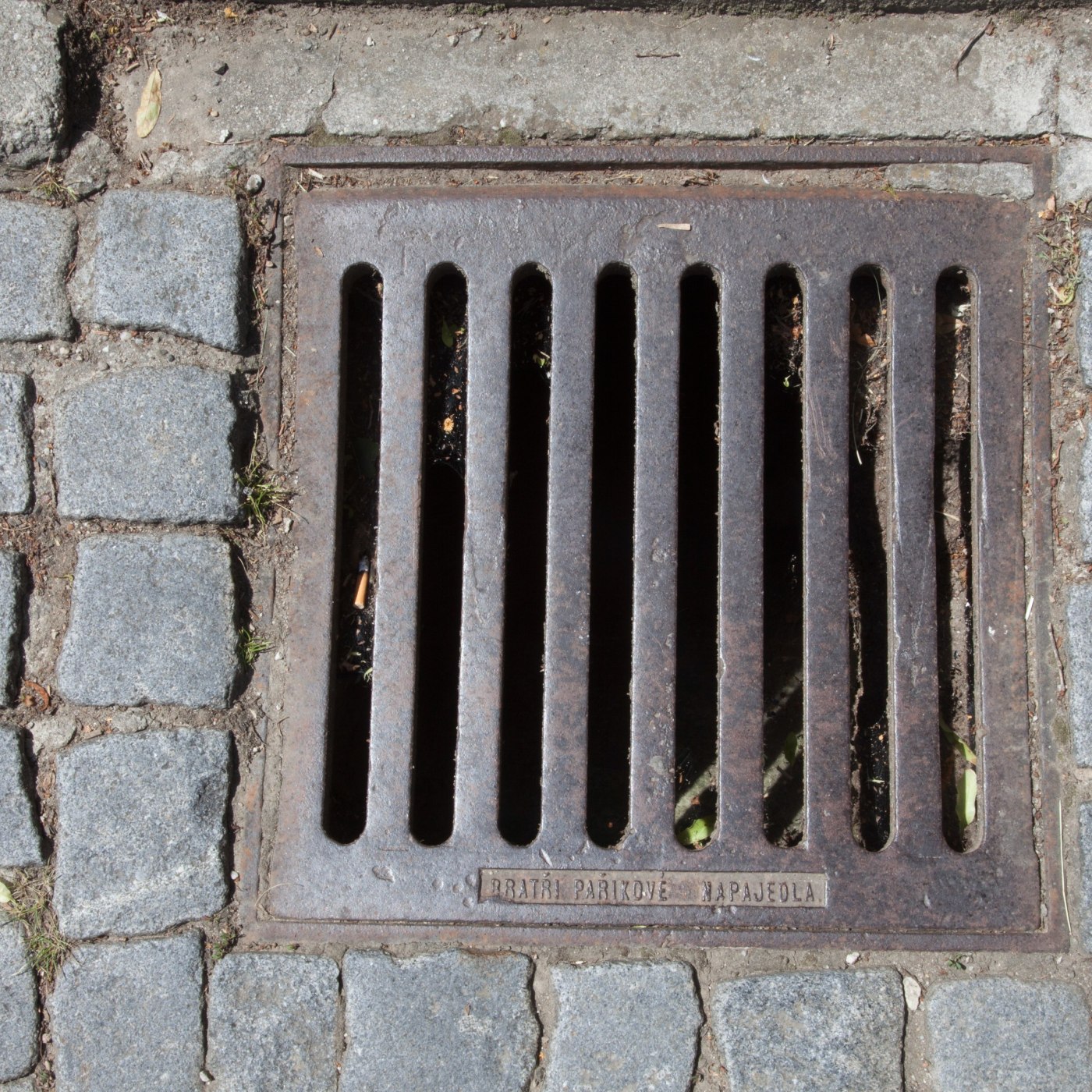 Obdélníková mříž s vertikálními lamelami je pečlivě zasazena do mozaiky žulových dlažebních kostek a betonového podkladu in Strážnice, Czechia — CoverSpot
