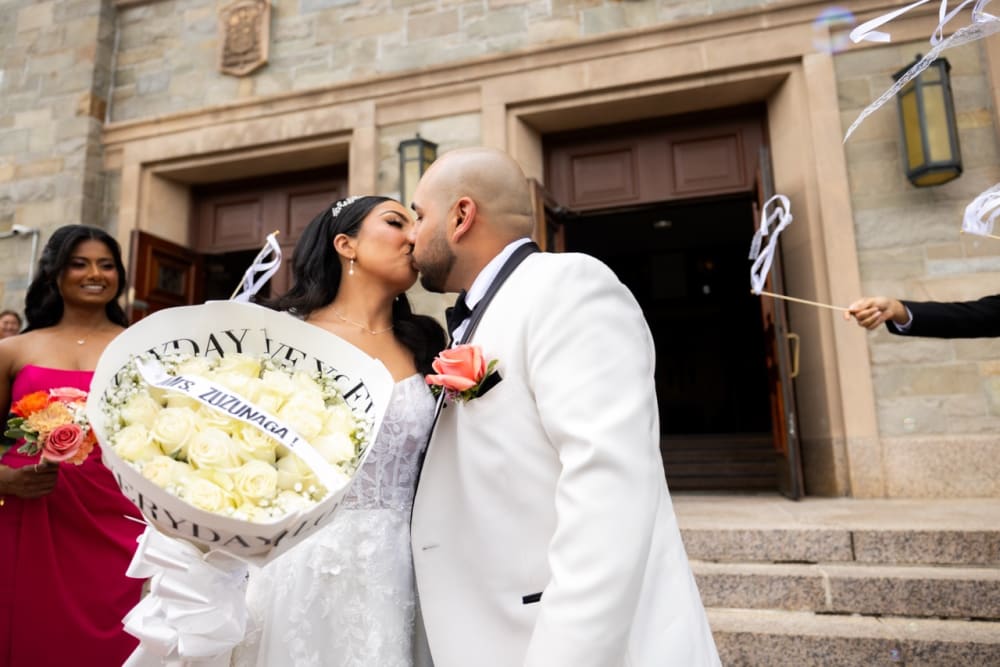 Newlyweds kissing on church steps with white roses