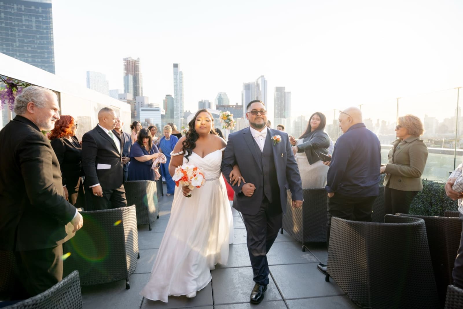 Newlyweds walking up a rooftop aisle with the Manhattan skyline behind them