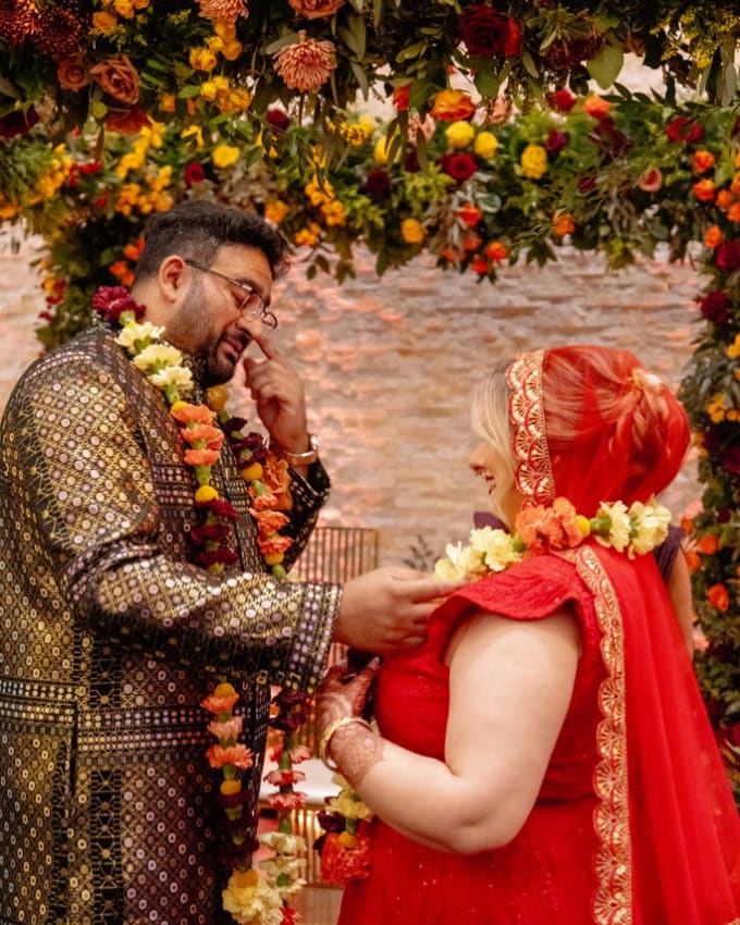 Couple exchanging garlands beneath a vibrant floral arch