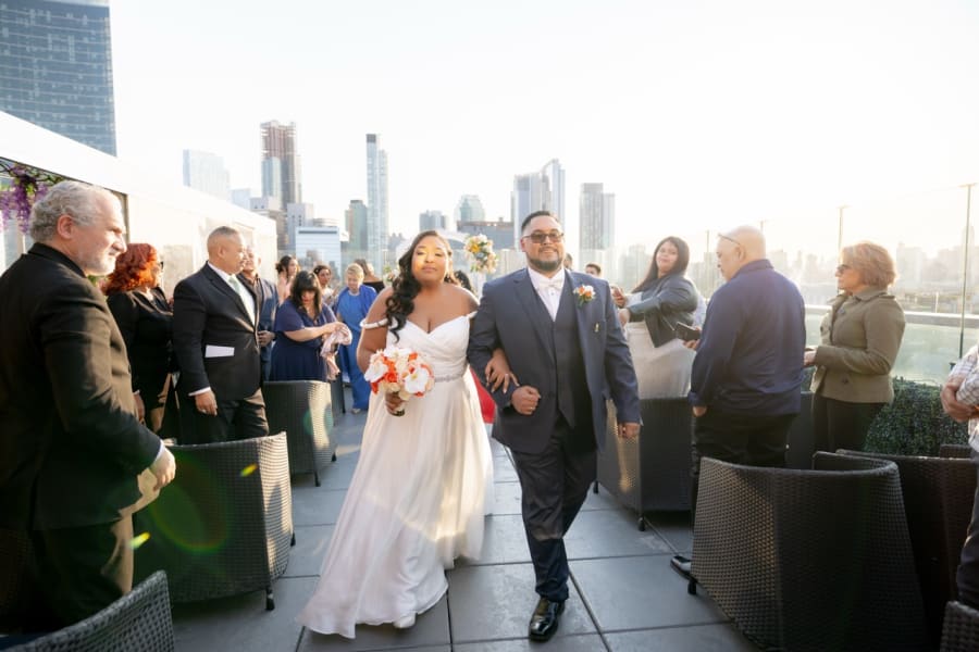 Bride walking down a rooftop aisle with the city skyline behind