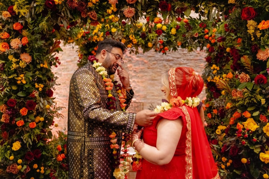 Couple exchanging garlands beneath a vibrant floral arch